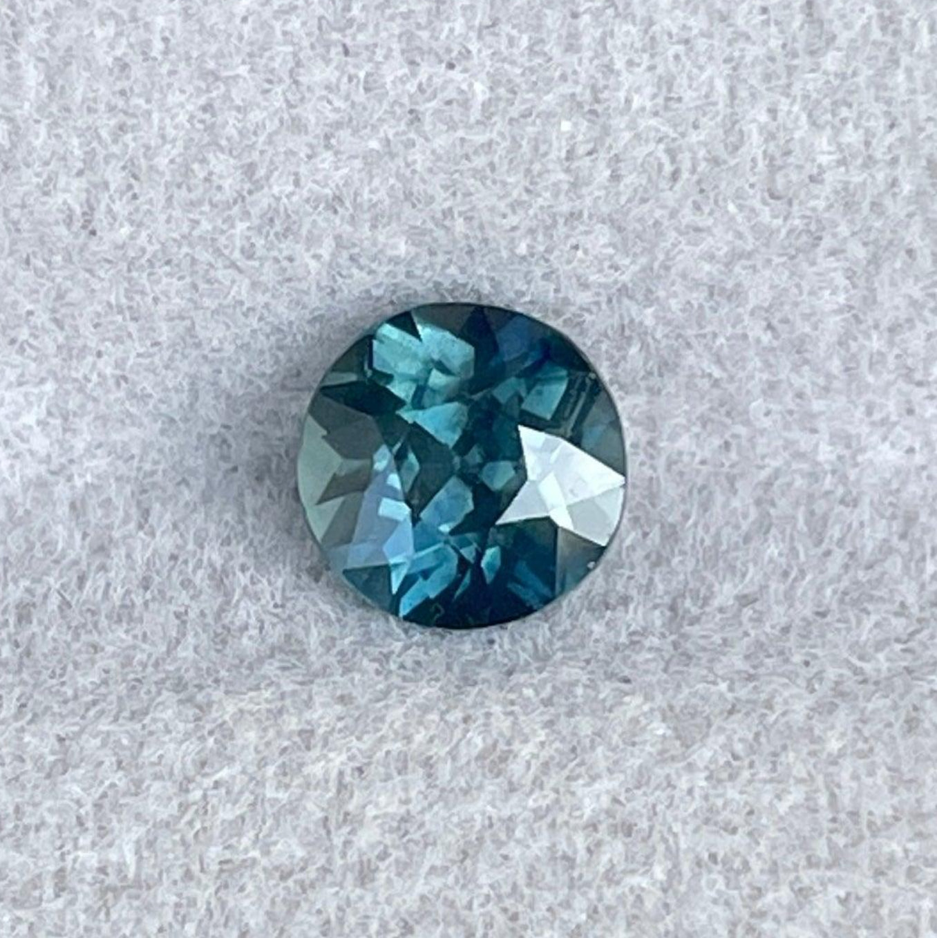 Saphir bleu-vert sarcelle taillé rond, 1,13 carats, serti dans une bague de fiançailles, mettant en valeur une couleur vibrante et les détails de la pierre précieuse.