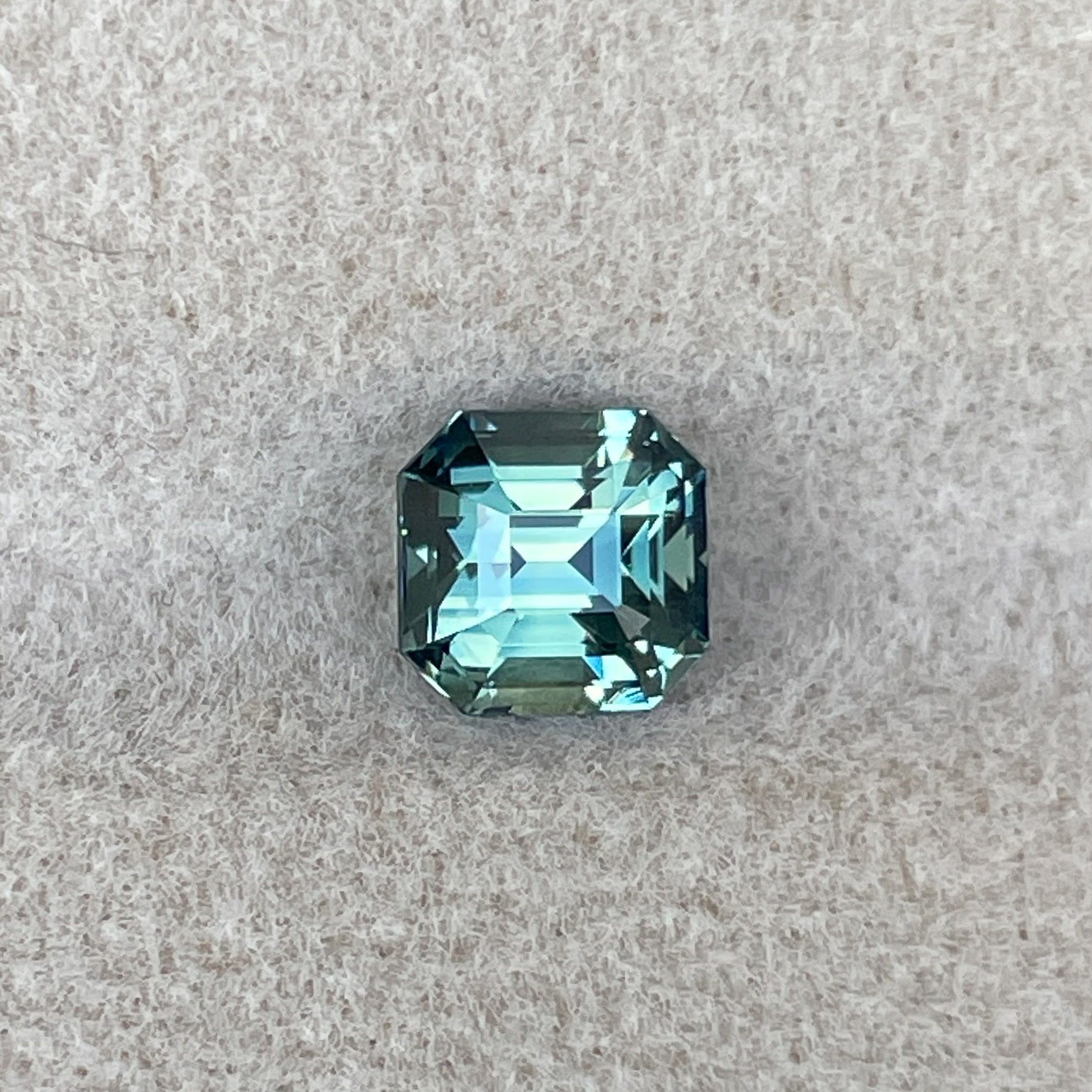 Teal green sapphire 1.36 Ct emerald cut from NASHGEMS, showcasing vibrant blue-green hues and a polished, faceted surface.