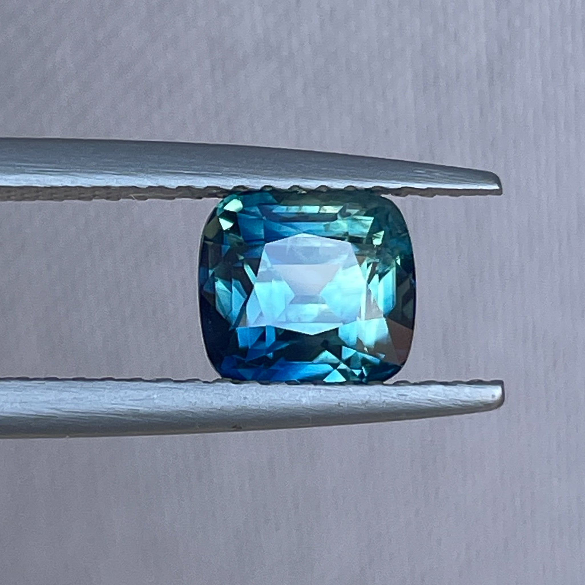 Natural teal sapphire cushion cut 2.14 Ct from NASHGEMS, showcasing vibrant blue-green hues and a brilliant faceted surface.