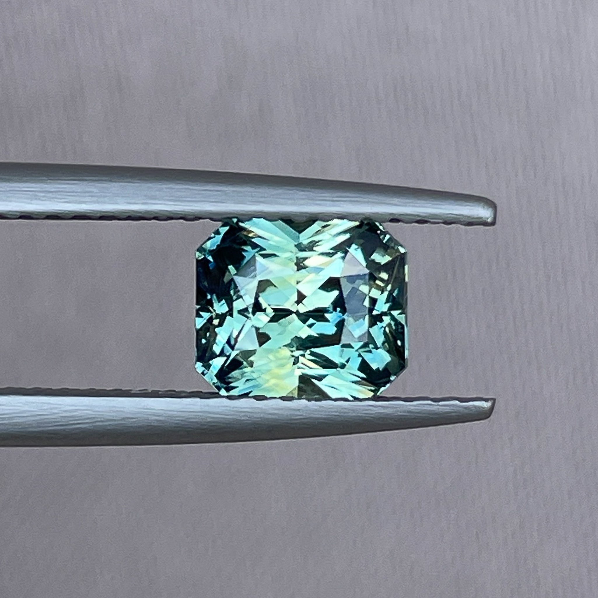 Teal sapphire loose gemstone in radiant cut, 1.65 carats, from NASHGEMS, showcasing vibrant blue-green color and sparkling facets.