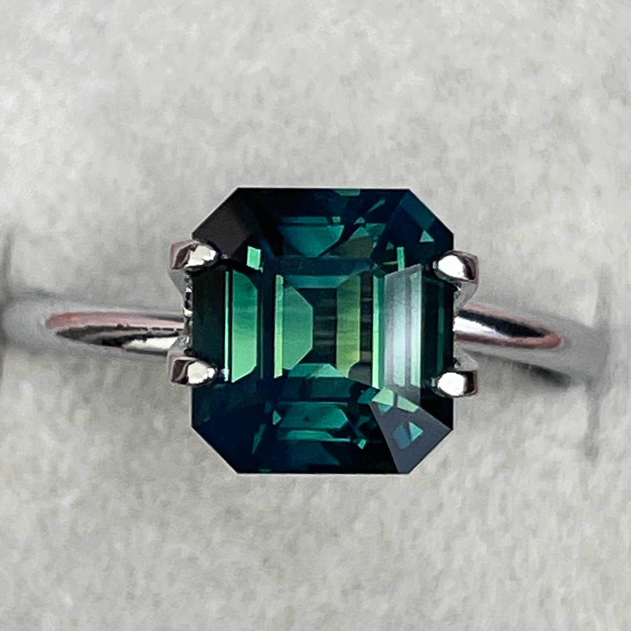 Natural forest green sapphire 3.59 ct emerald cut loose gemstone by NASHGEMS, showcasing deep teal color and high clarity.
