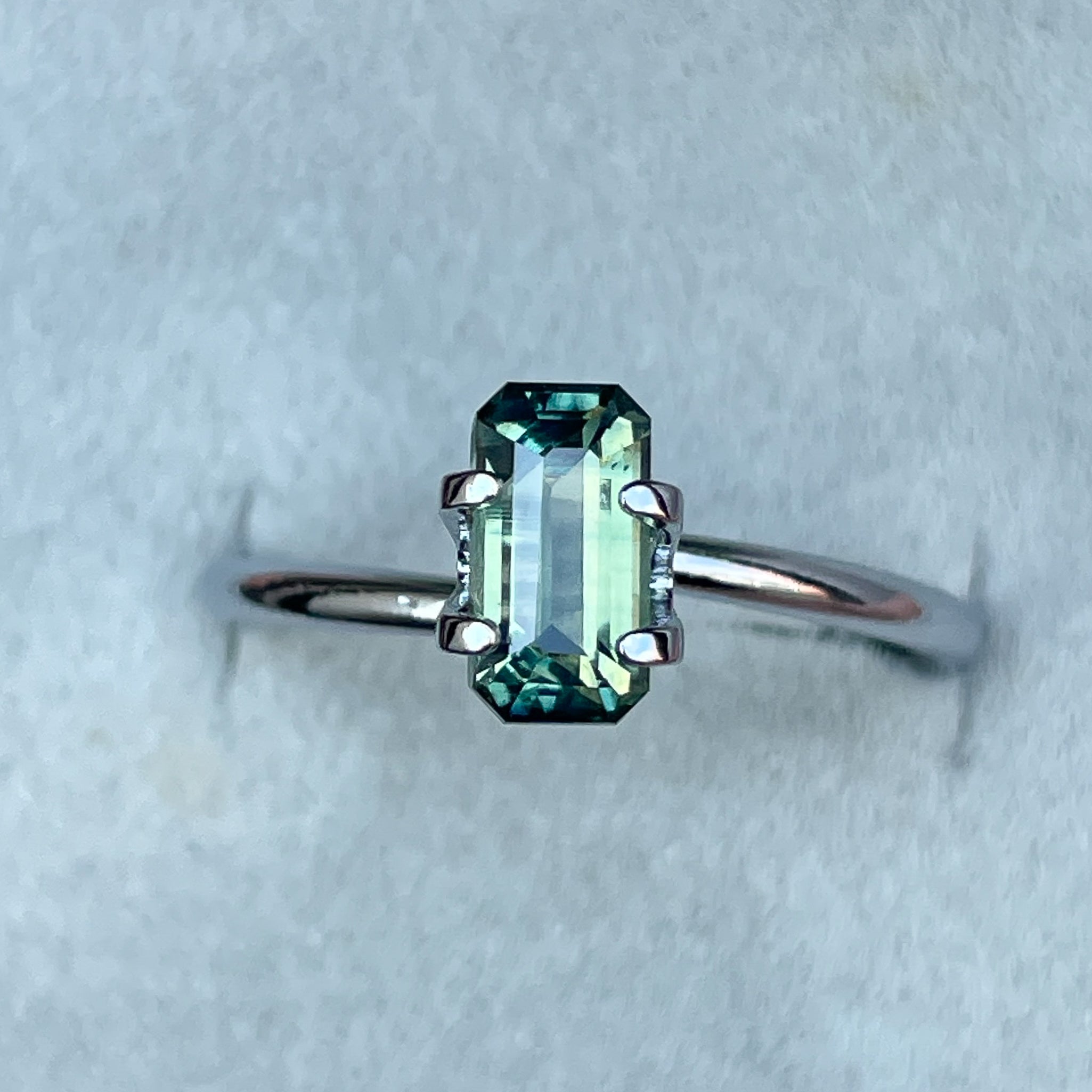 Teal sapphire loose gemstone with emerald cut, 1.49 carats, vibrant green and blue hues, from NASHGEMS, perfect for September birthstone jewelry.