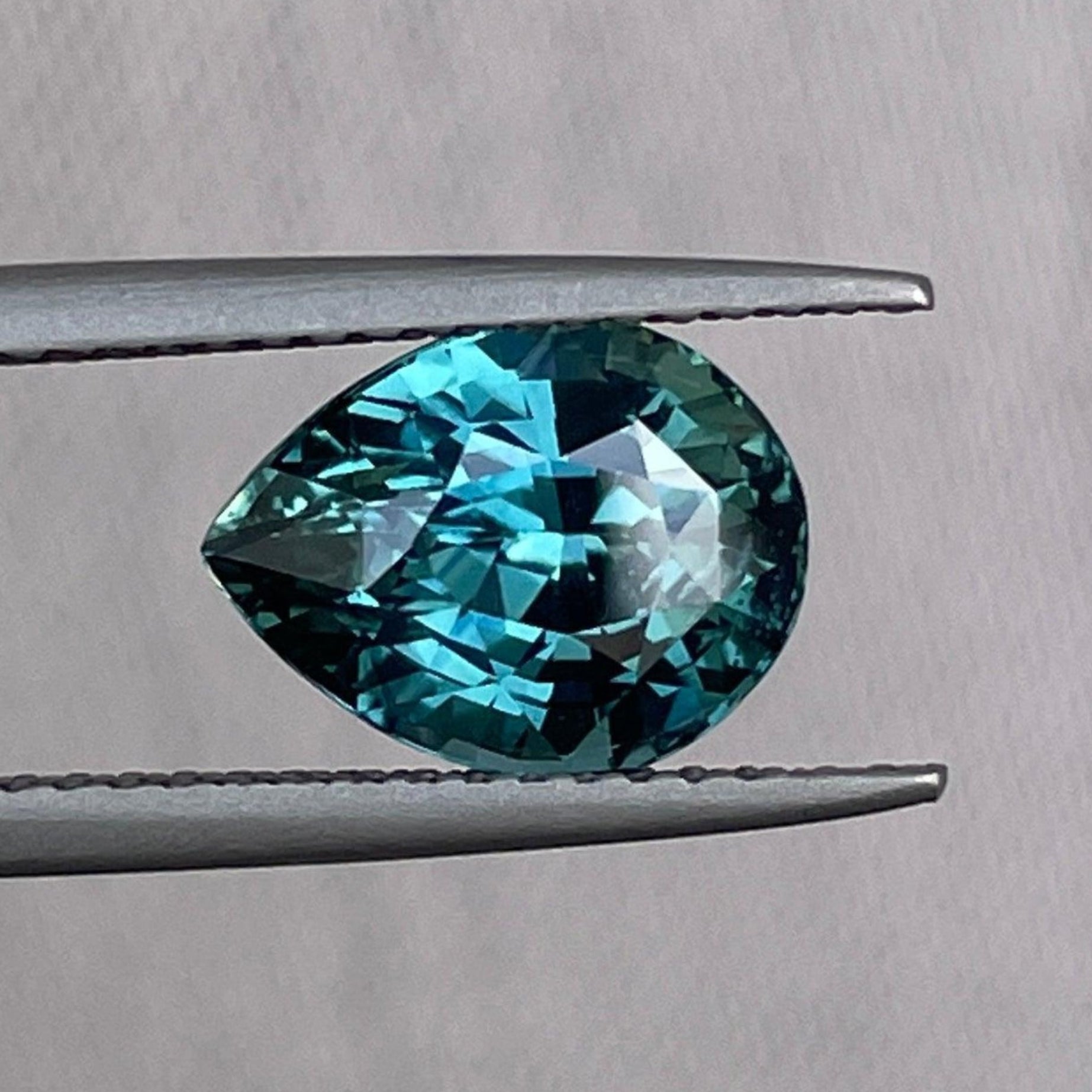 Teal sapphire gemstone in a pear drop shape with blue-green hues, crafted by NASHGEMS, showcasing vibrant color and clarity.
